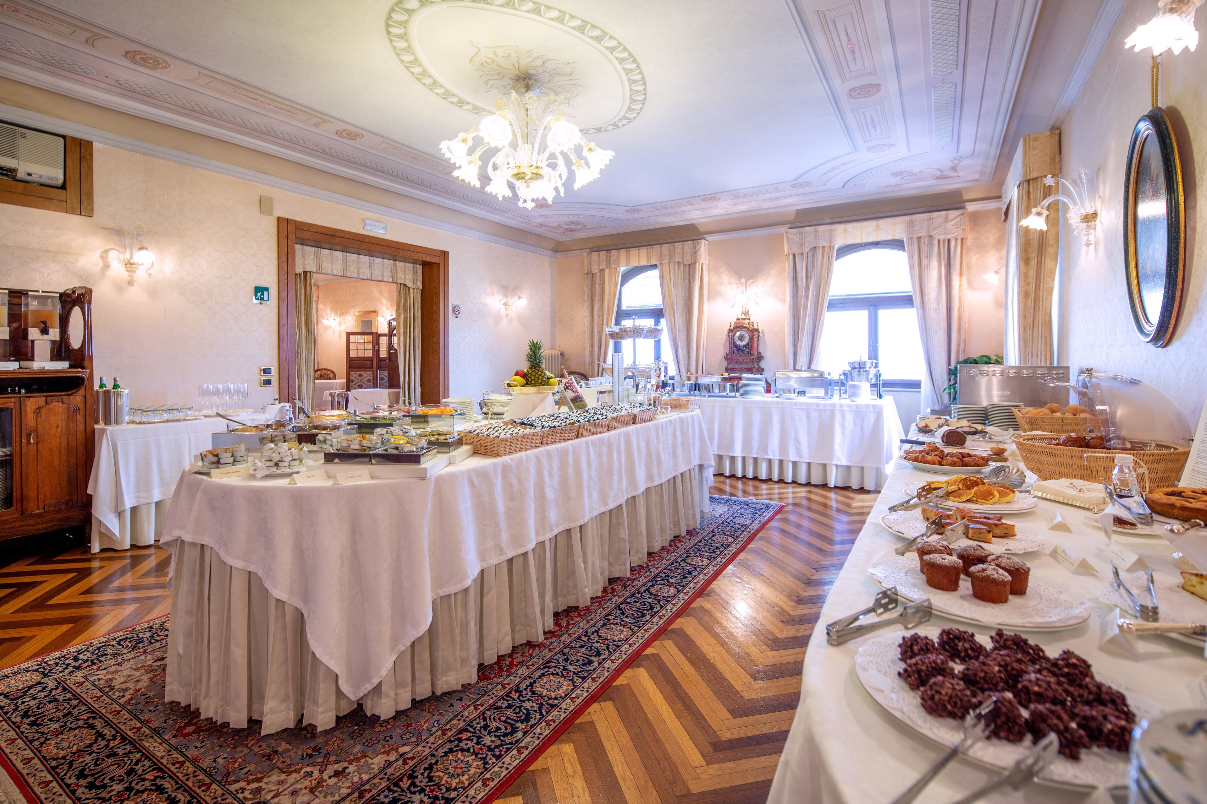 Una sala da banchetti con un lungo tavolo ricoperto da tovaglie bianche, circondato da diverse pietanze e un grande specchio sulla parete.