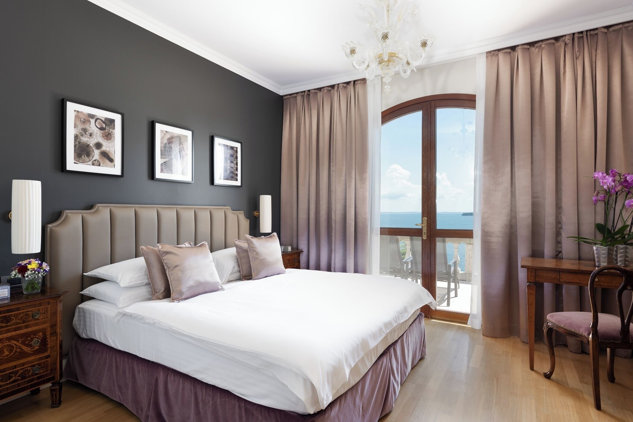 A bedroom with a large bed, a nightstand, a chair, a table, and a view of the outdoors.