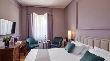 Une chambre d’hôtel avec un grand lit, deux chaises, une petite table avec un vase, une télévision et une lampe.