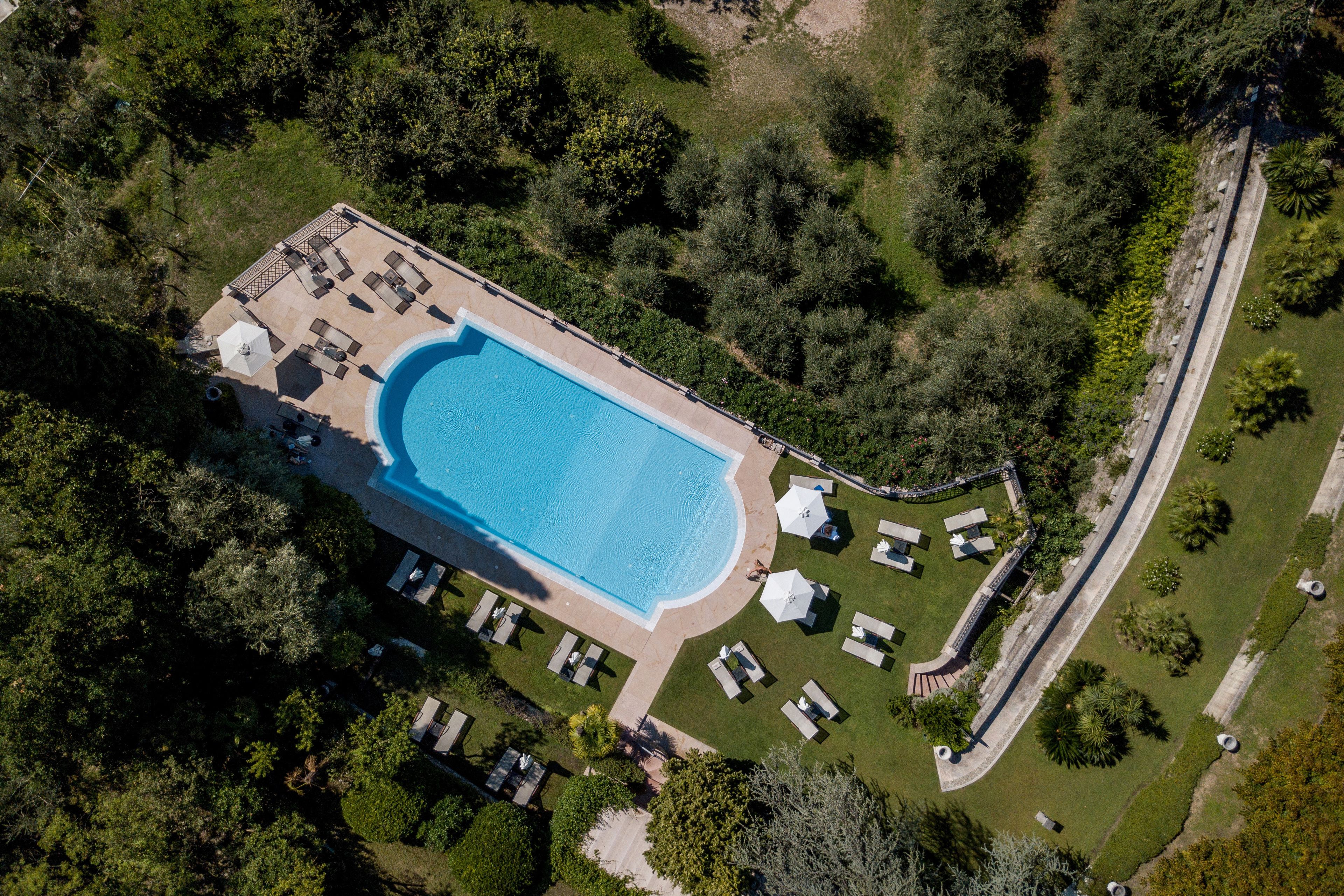An aerial view of a resort with a swimming pool, sun loungers, and a well-maintained lawn.