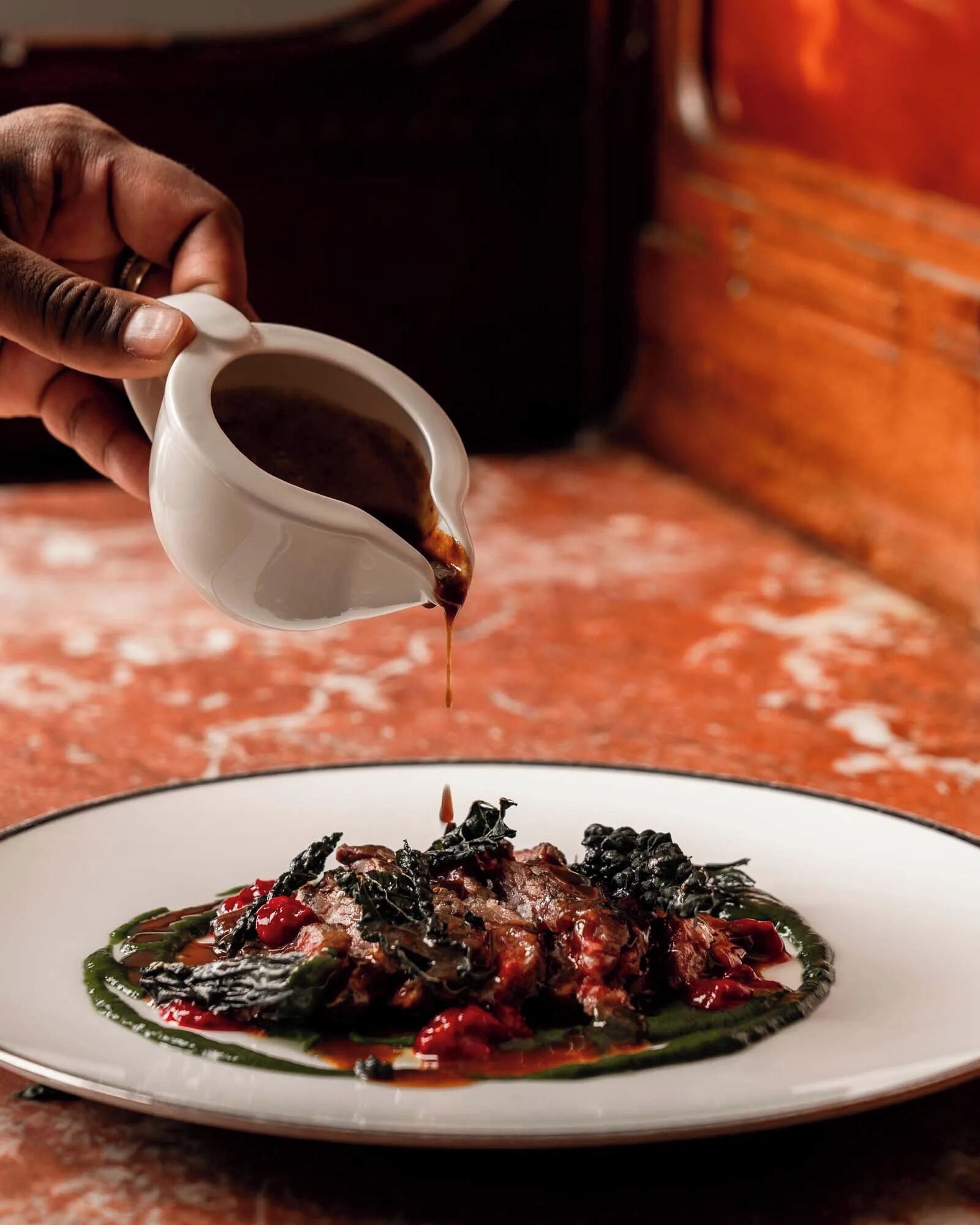 A hand pouring sauce over a dish on a plate.