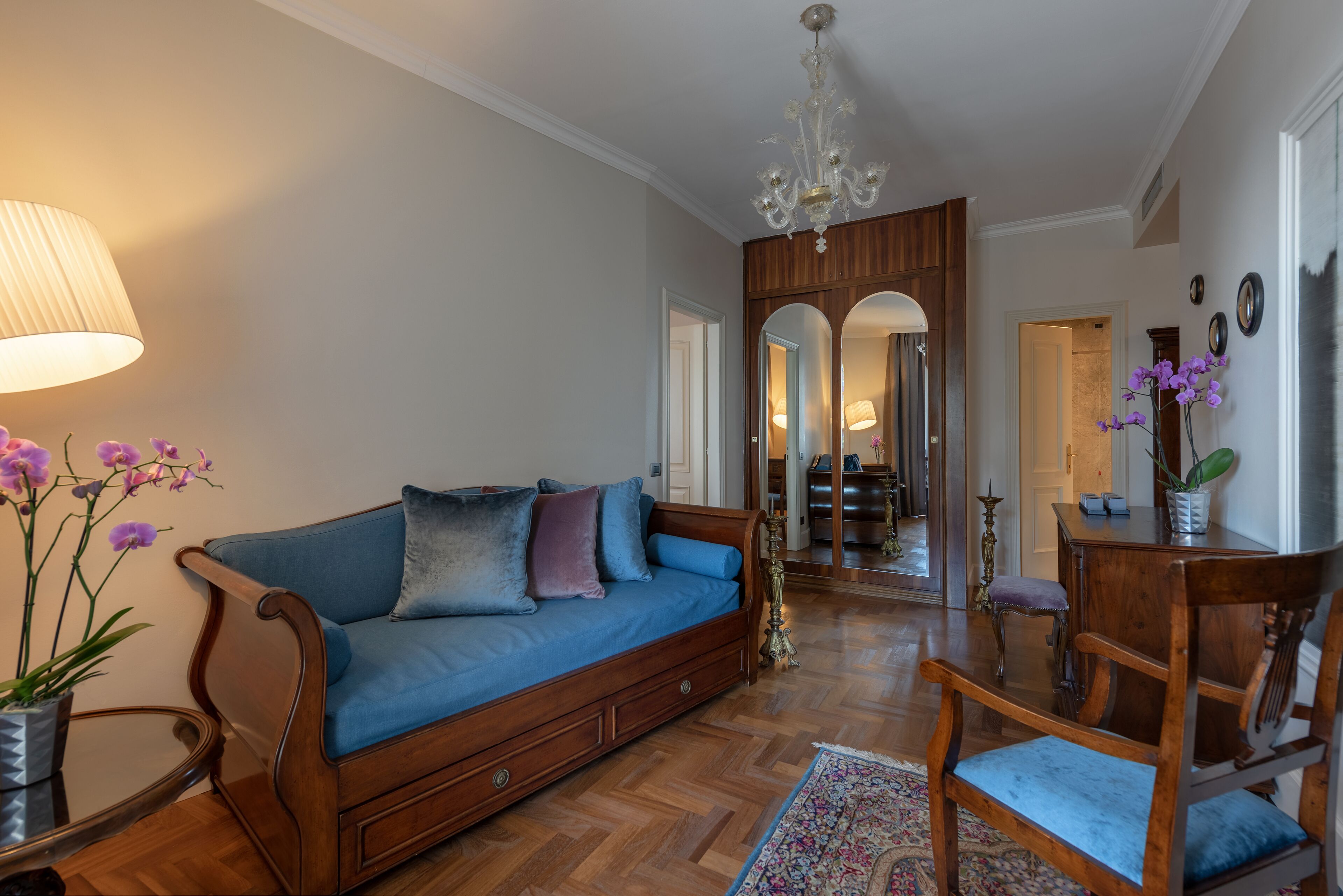 A living room with a blue sofa, wooden furniture, a chandelier, and a mirror reflecting the room.