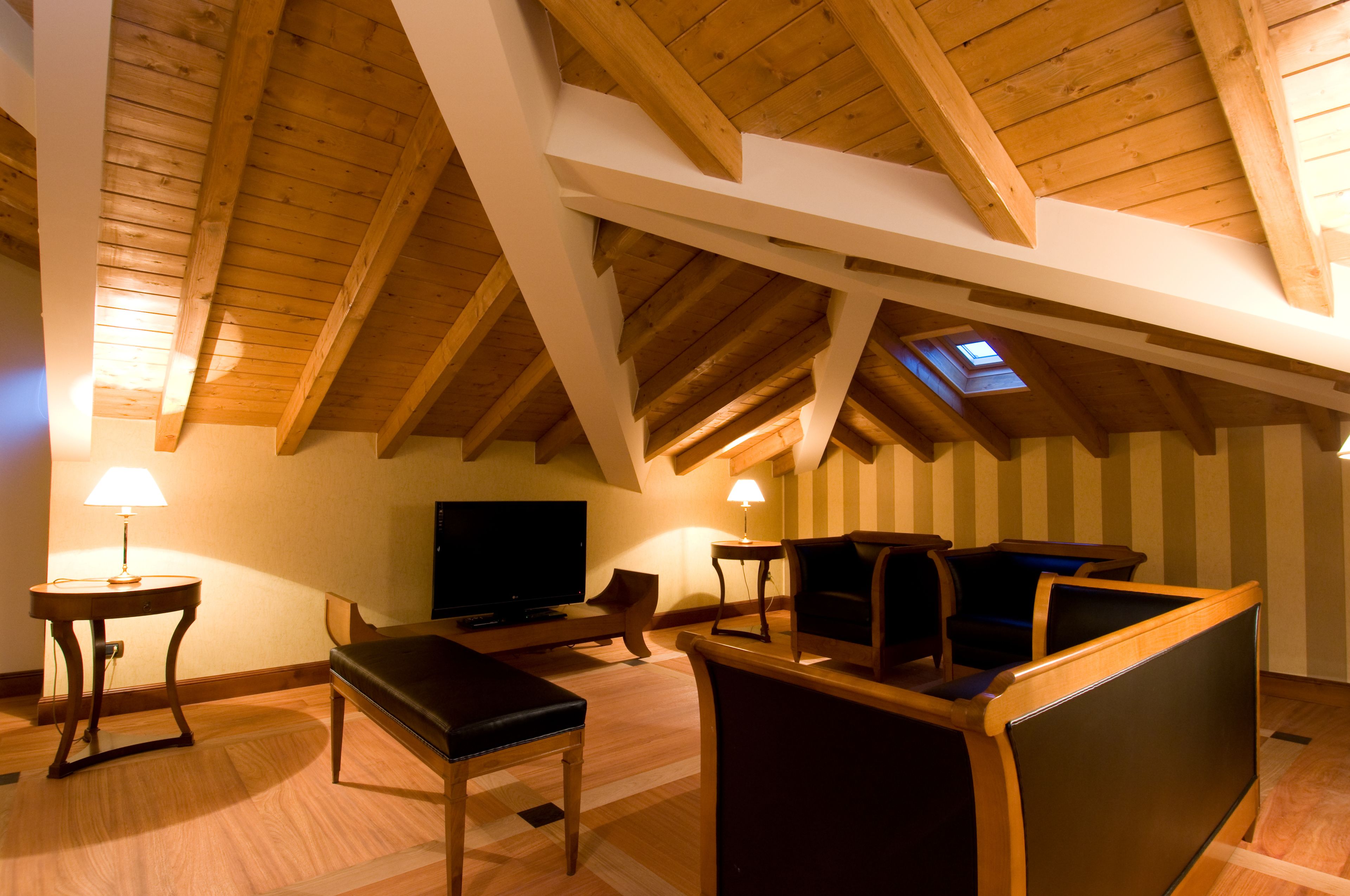 An attic room with wooden beams, a television, seating, and a skylight.