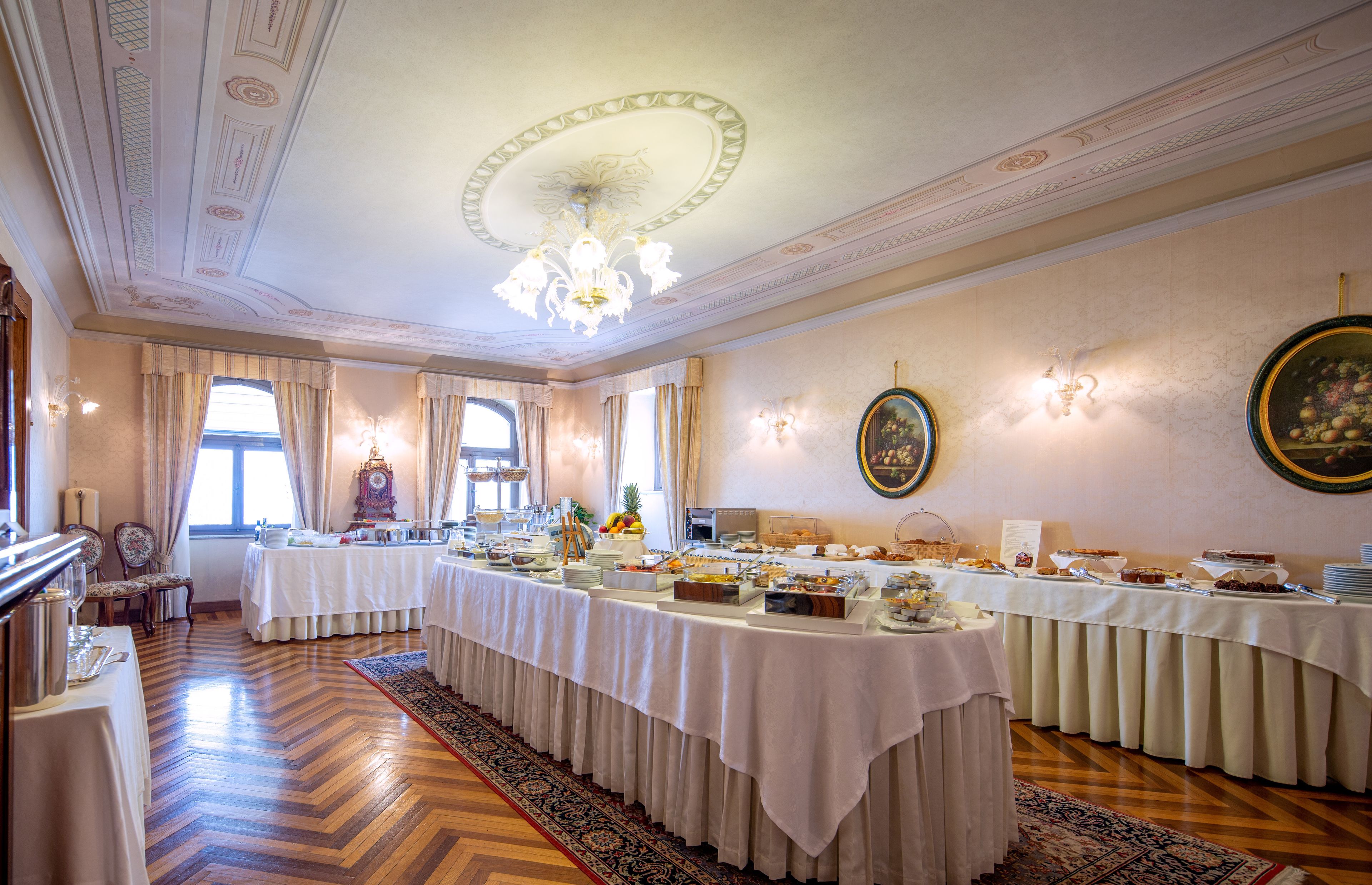 A formal dining room with a long table set for a buffet, elegant chandeliers, and classic decor.