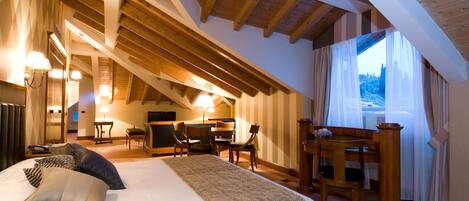 A bedroom with a large bed, a desk, and a chair, wooden beams on the ceiling, and a window with curtains.