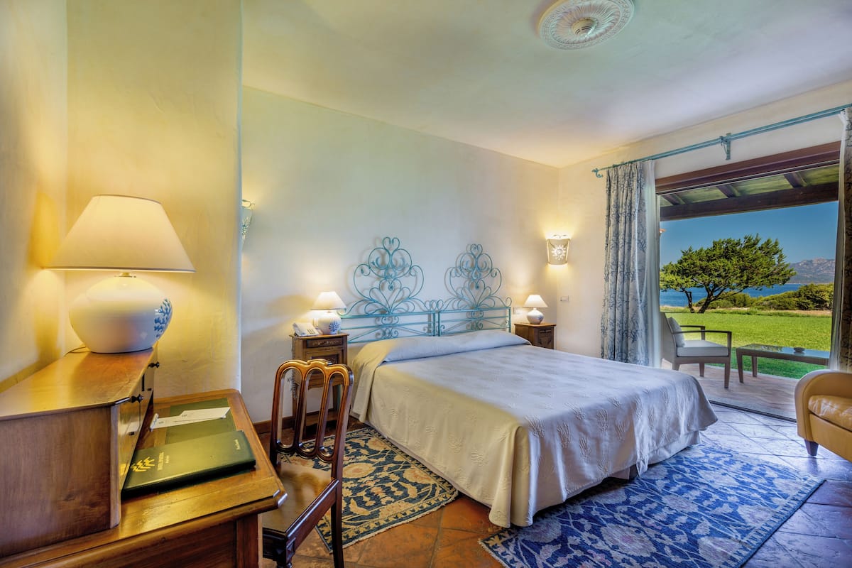 Une chambre à coucher avec un lit, des lampes de chevet, un bureau et une chaise. Une fenêtre offre une vue sur l’extérieur.