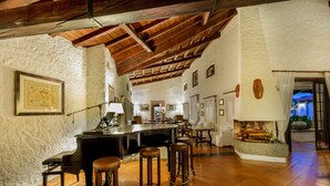 A bar area with a piano, stools, and a rustic interior with exposed wooden beams and a tiled floor. - Hotel Sporting (Olbia)