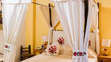 A four-poster bed with white linens and floral pillows, a wooden ceiling, and a yellow wall.