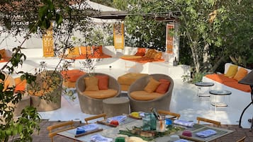 An outdoor patio with wicker furniture, a dining table set with various items, and a white wall in the background.