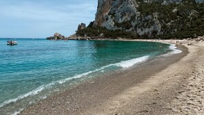 Una playa con aguas turquesas cristalinas, acantilados rocosos y una orilla pedregosa.