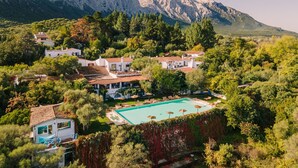 Una propiedad en una colina con piscina, varias construcciones y montañas al fondo.