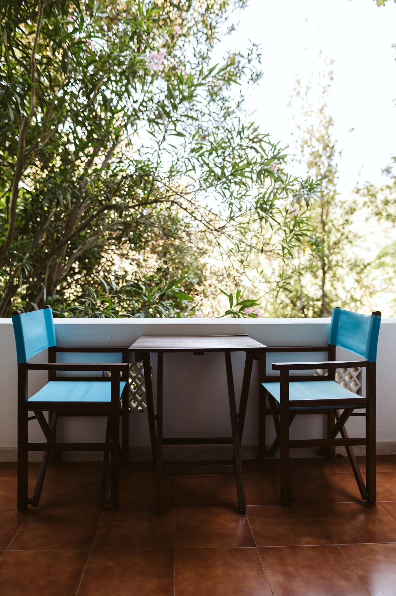 A patio with two wooden chairs and a table, surrounded by greenery.