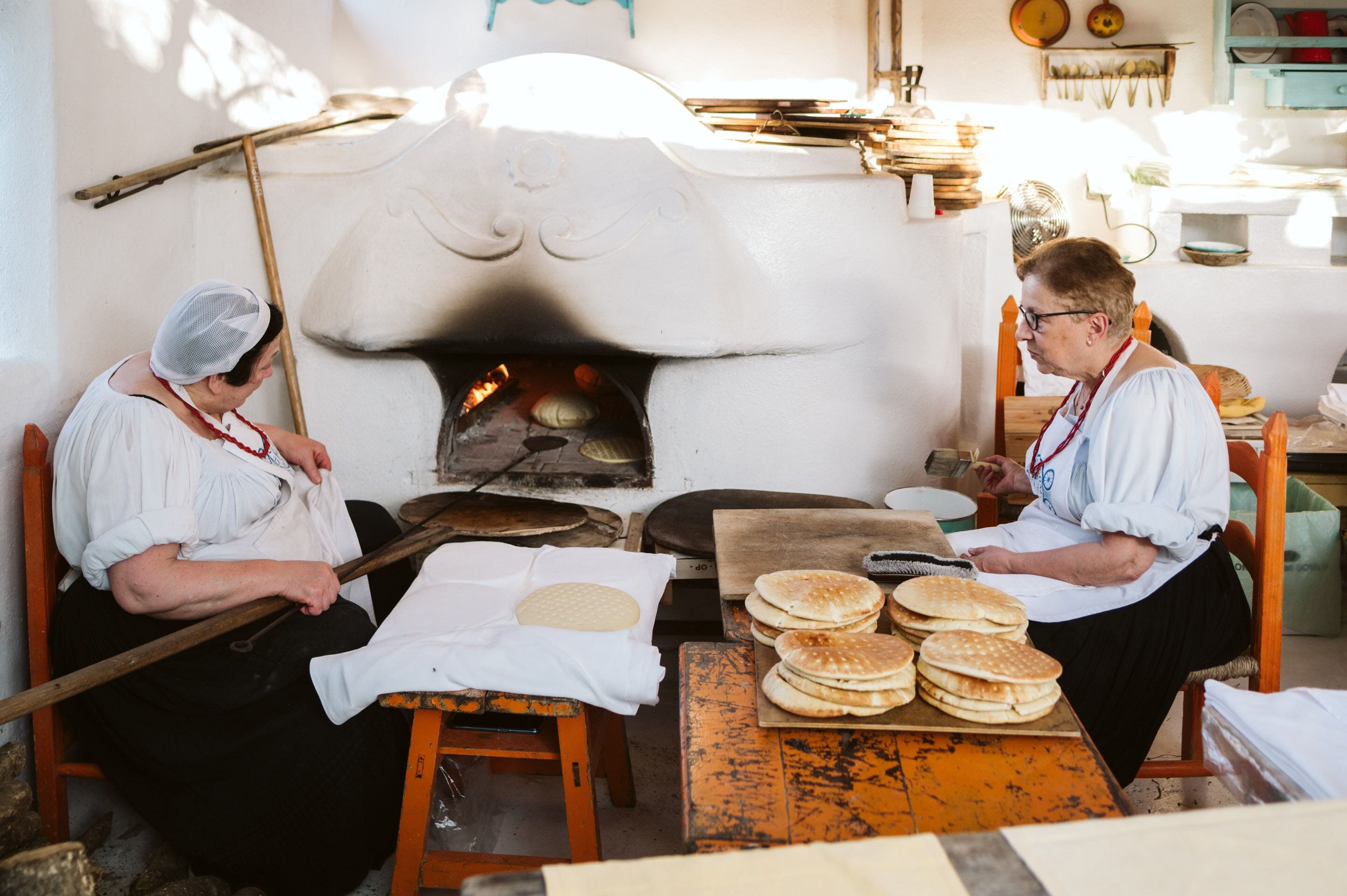 A traditional bakery with a wood-fired oven, dough on a table, and a woman working.