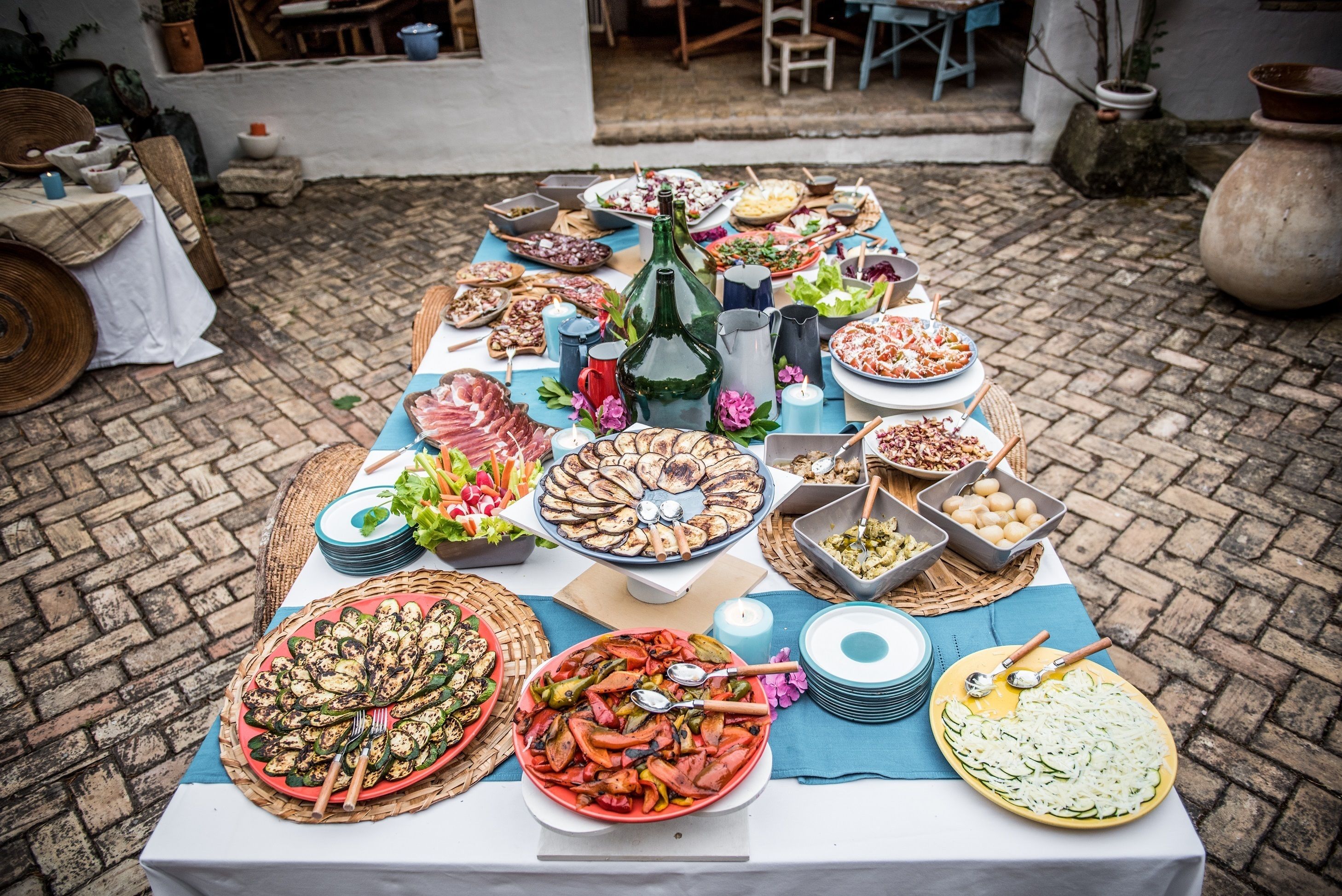 A table set outdoors with various dishes and drinks, surrounded by wicker chairs and a rustic setting.