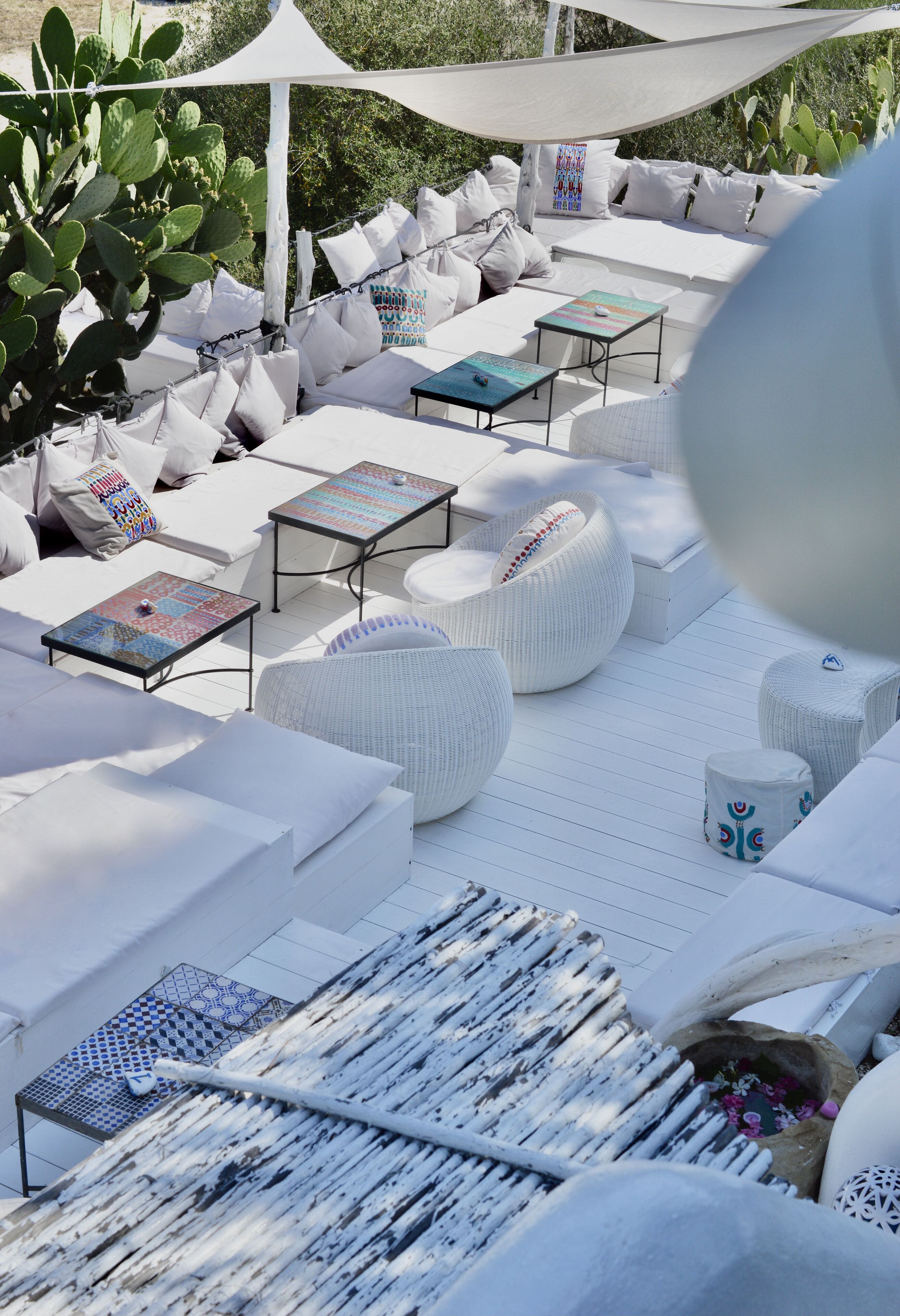 An outdoor lounge area with white sofas, round seating, and small tables.