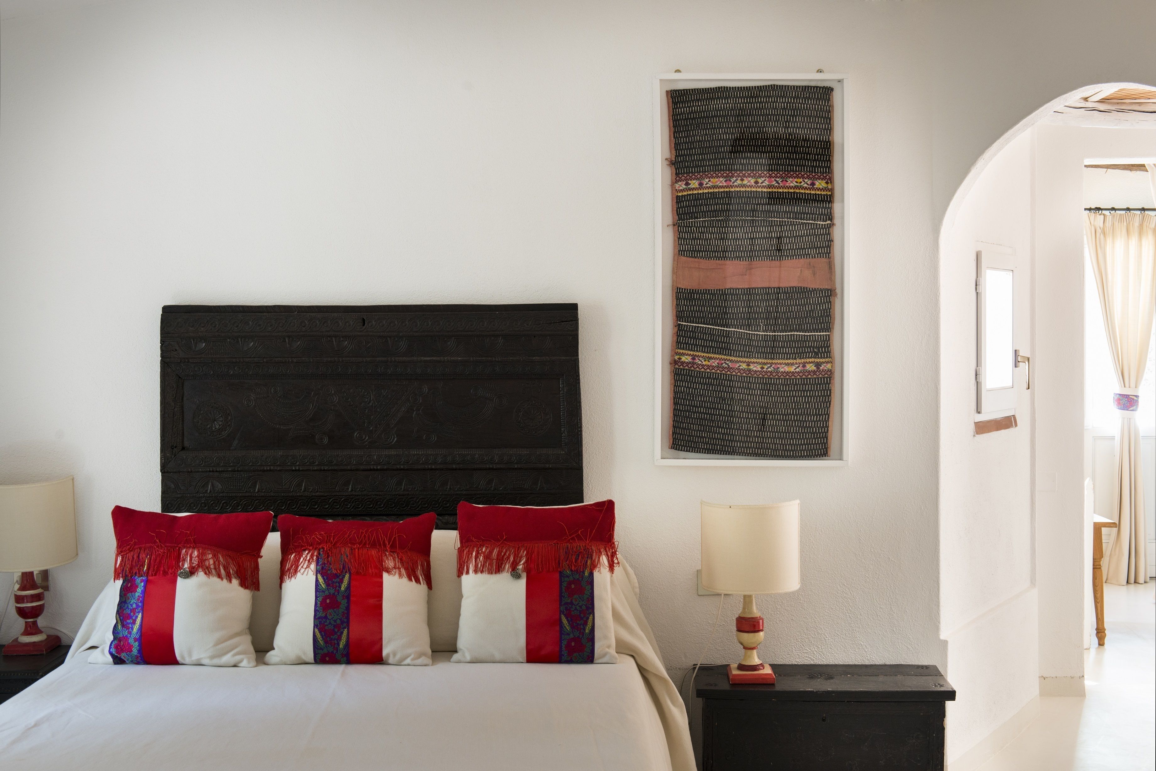 A neatly made bed with red and white pillows, a dark headboard, and a wall-mounted tapestry.