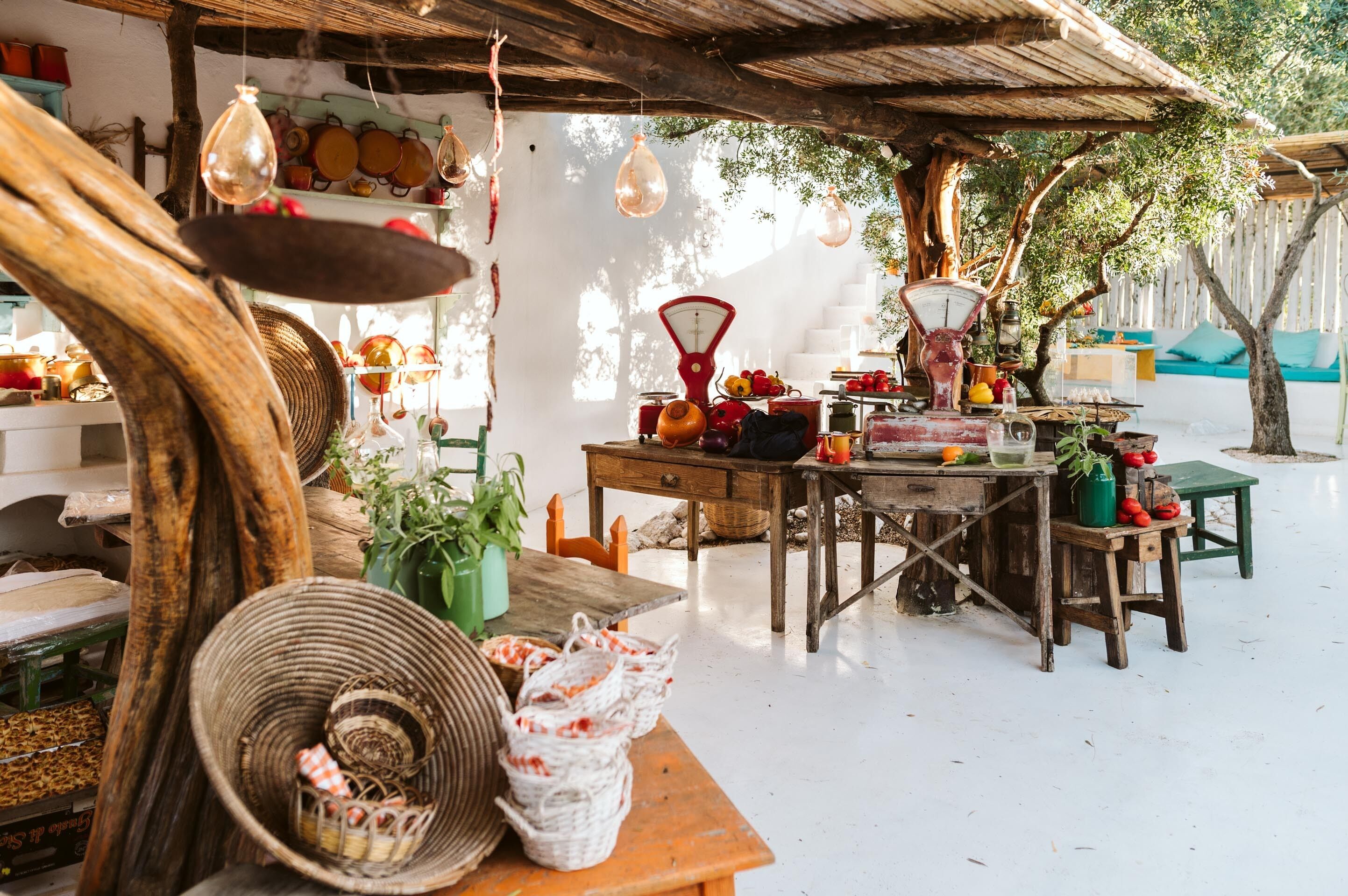 Ein rustikaler Markt im Freien mit Holztischen, hängenden Lichtern und verschiedenen Waren zum Verkauf.