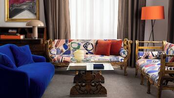 A living room with a blue sofa, a patterned sofa, a glass coffee table, and a lamp.