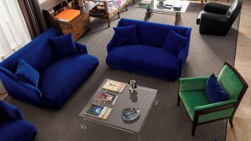 Un salón moderno con sofás azules, un sillón verde y una mesa de centro de vidrio.