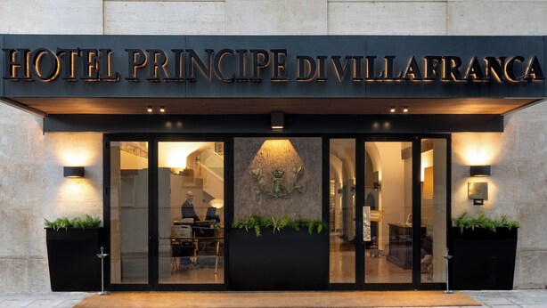 Het uiterlijk van Hotel Principe Divillafranca, met een moderne gevel, verlichte reclameborden en een gastvrije entree.