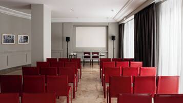 Una sala conferenze con sedie rosse, uno schermo per proiettore e un'ampia finestra con tende.