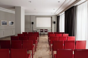 Une salle de conférence avec des chaises rouges, un écran de projection et une grande fenêtre avec des rideaux.