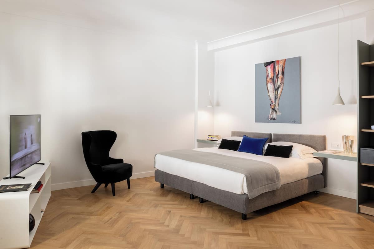 A modern bedroom with a large bed, a black chair, a TV, and a painting on the wall.