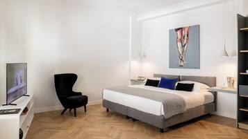 Une chambre à coucher moderne avec un grand lit, une chaise noire, un téléviseur et un tableau accroché au mur.