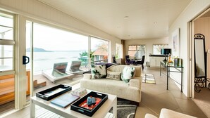 A spacious living area with a large window overlooking a scenic view, a cozy seating area with a sofa and chairs, and a kitchen in the background. - On The Point - Lake Rotorua (Rotorua)