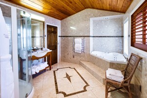 Casa de banho com cabine de chuveiro em vidro, toucador de madeira, banheira e cadeira de vime com toalhas.