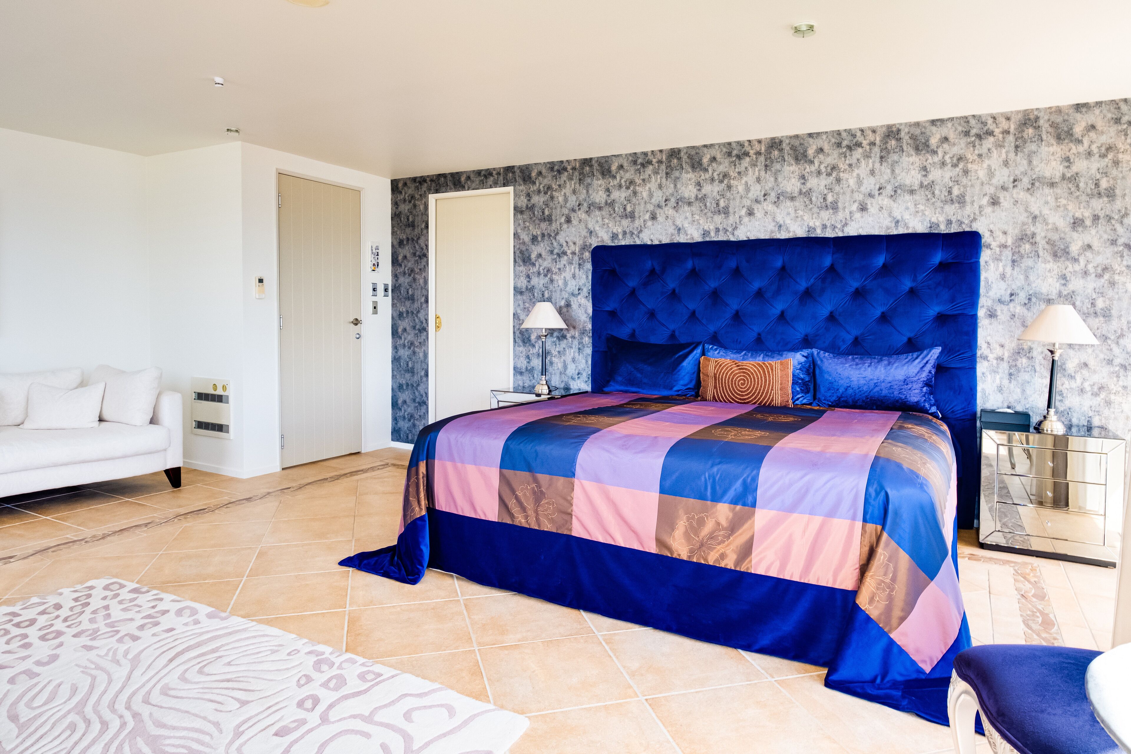 A bedroom with a large bed, a white sofa, and a patterned rug.