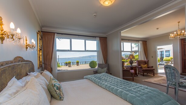 A bedroom with a large bed, a view of the sea, and a balcony with outdoor furniture. - On The Point - Lake Rotorua (Rotorua)
