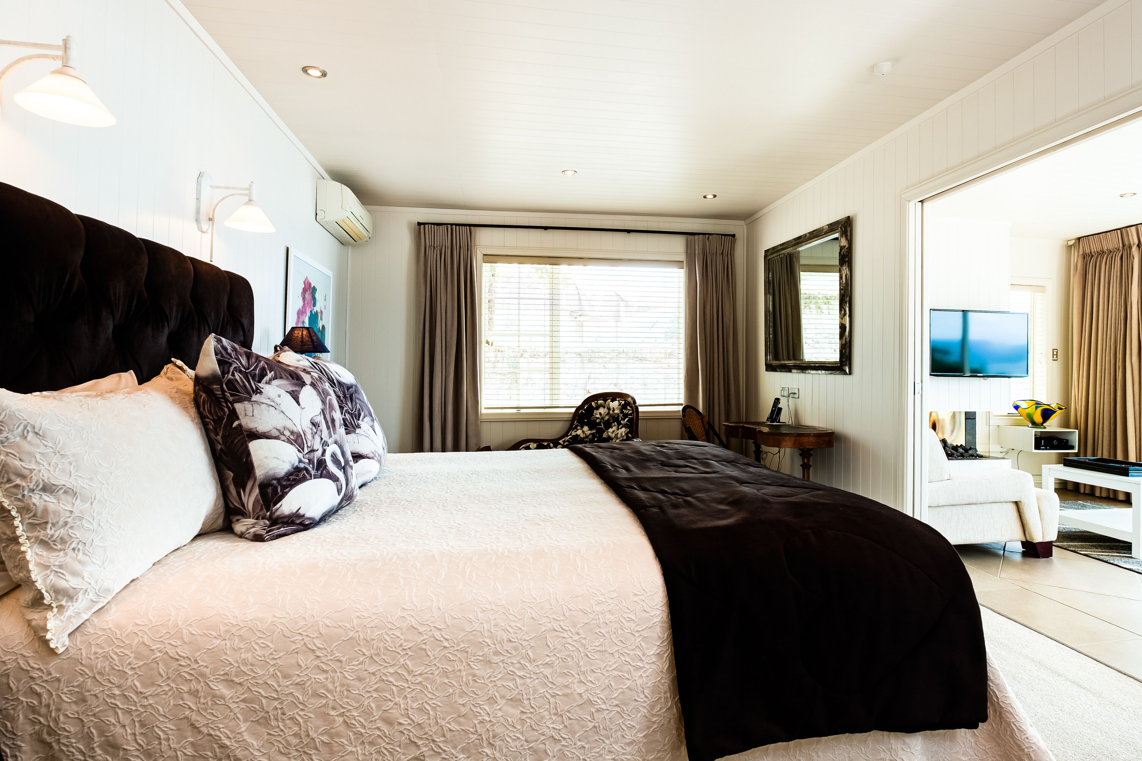 A hotel room with a large bed, a desk, a chair, a TV, and a window with curtains.