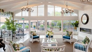 A spacious indoor area with white wicker furniture, large windows, and a view of the outside. - On The Point - Lake Rotorua (Rotorua)