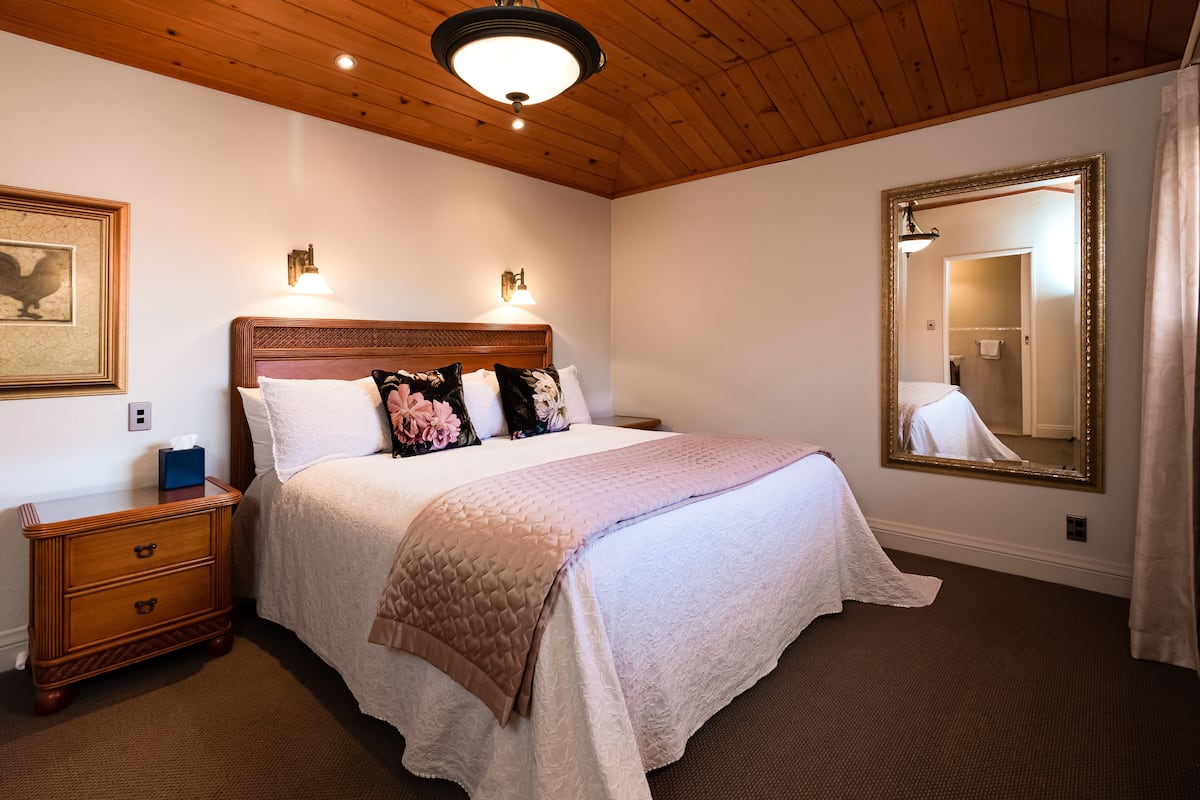 Un dormitorio ordenado con una cama grande, mesitas de noche, un espejo y una lámpara en el techo.