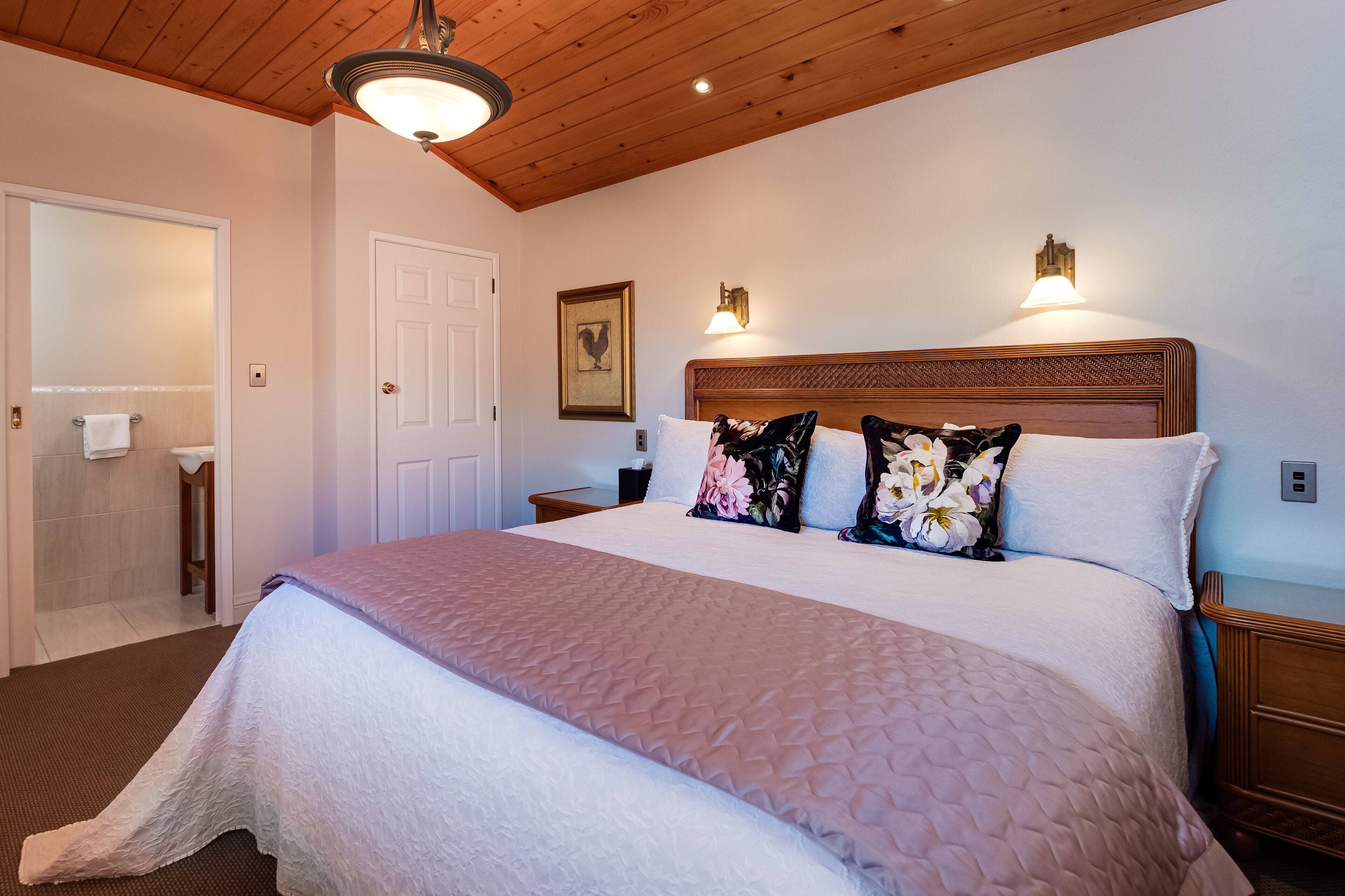 A neatly made bed with a quilted cover, a wooden headboard, and two wall-mounted lights.