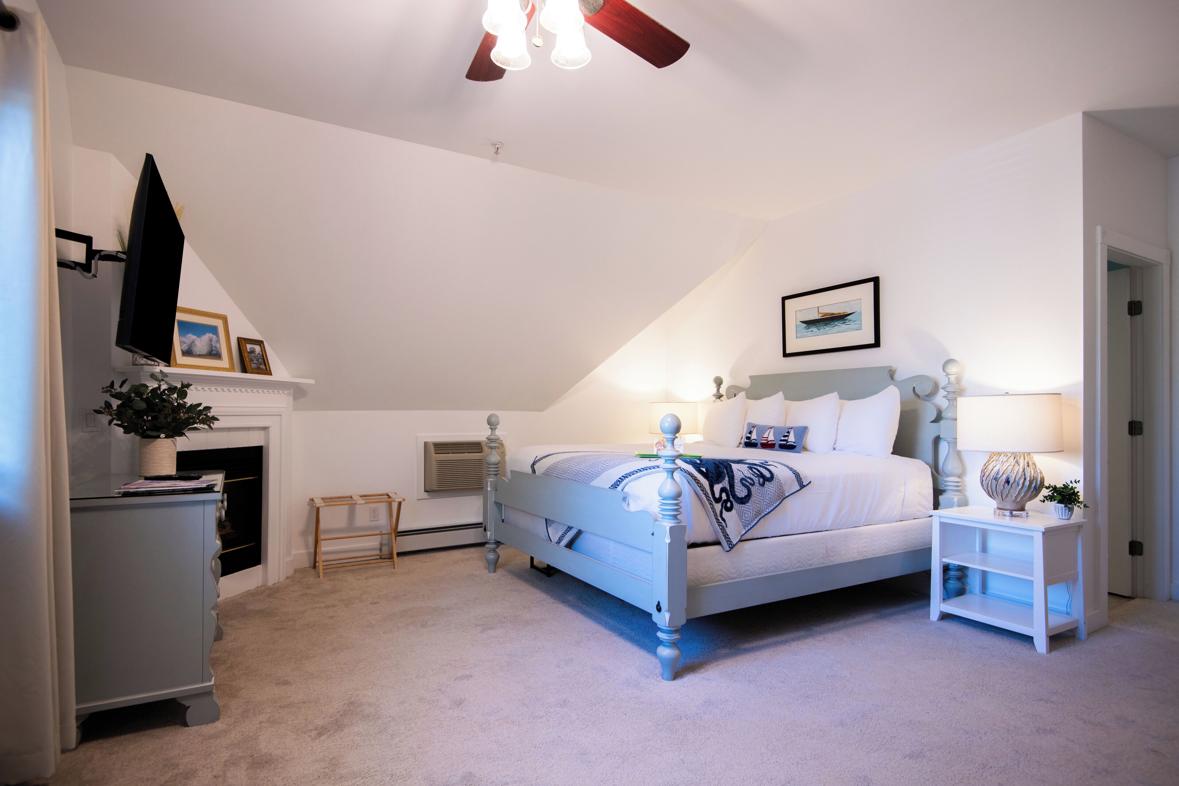 Une chambre à coucher comprenant un lit, des tables de chevet, une commode, un ventilateur de plafond et une cheminée.