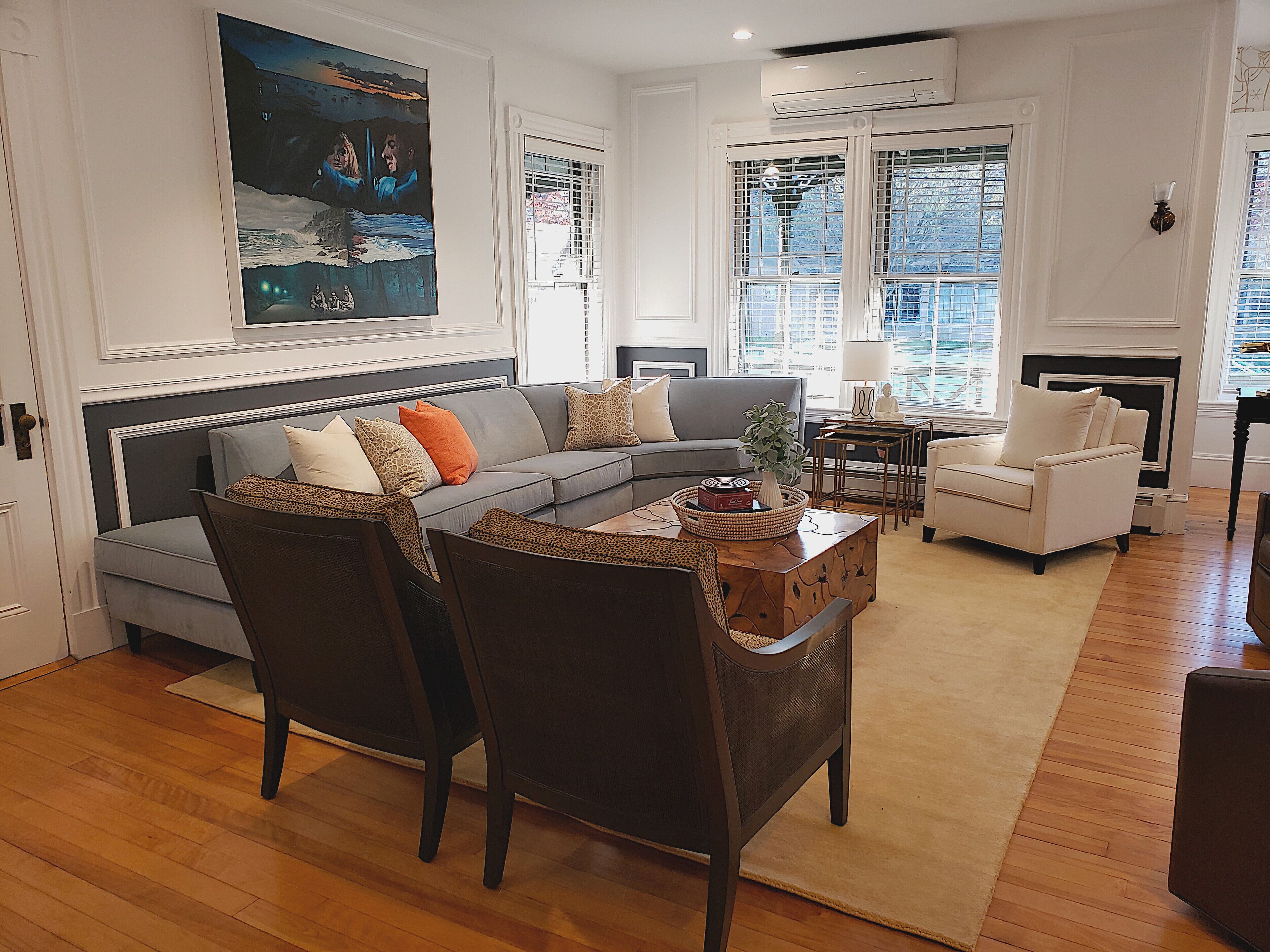 A living room with a grey sofa, two armchairs, a coffee table, and a painting on the wall.