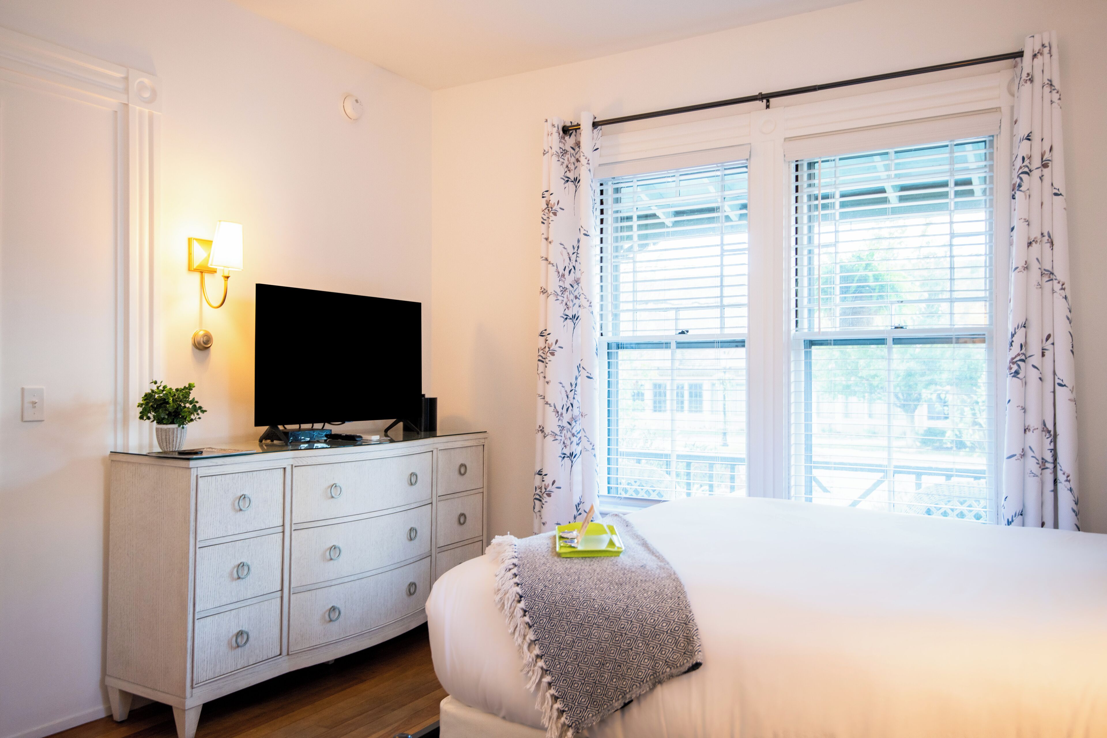 A bedroom with a bed, a dresser with a TV, and a window with curtains.