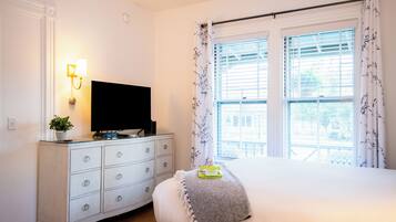 A bedroom with a bed, a dresser with a TV, and a window with curtains.