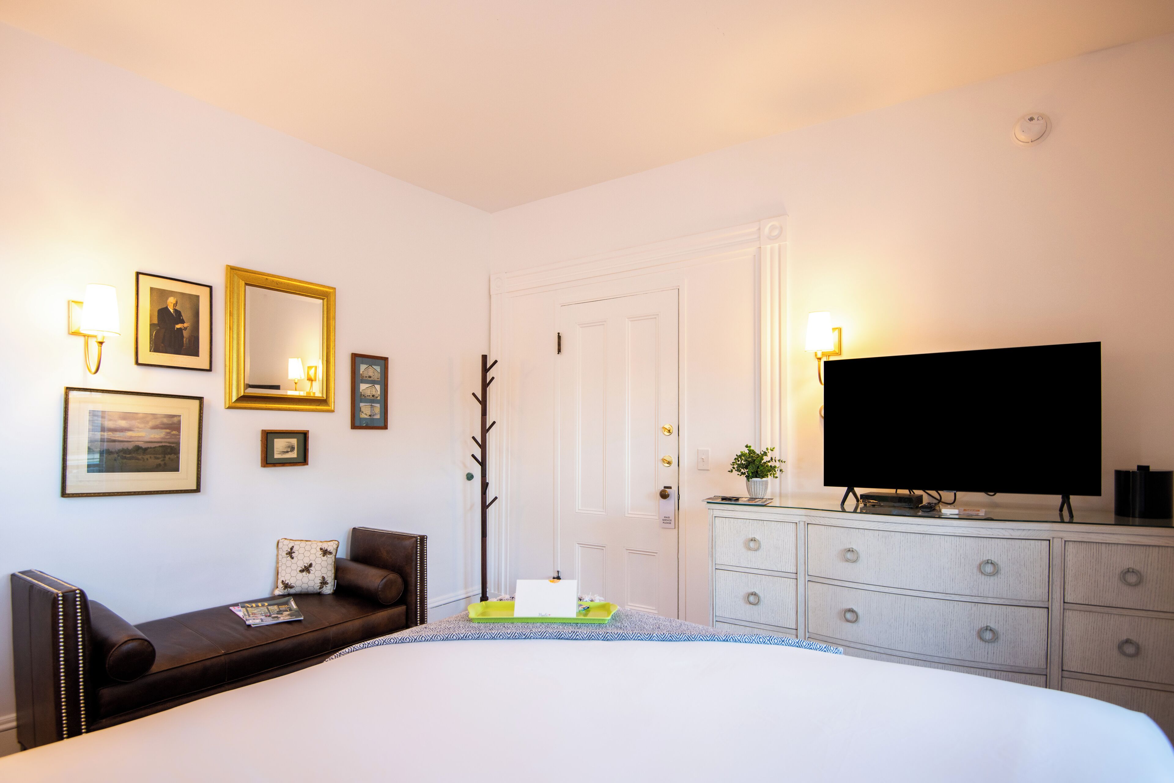 A bedroom with a bed, a dresser, a television, and wall-mounted lamps.
