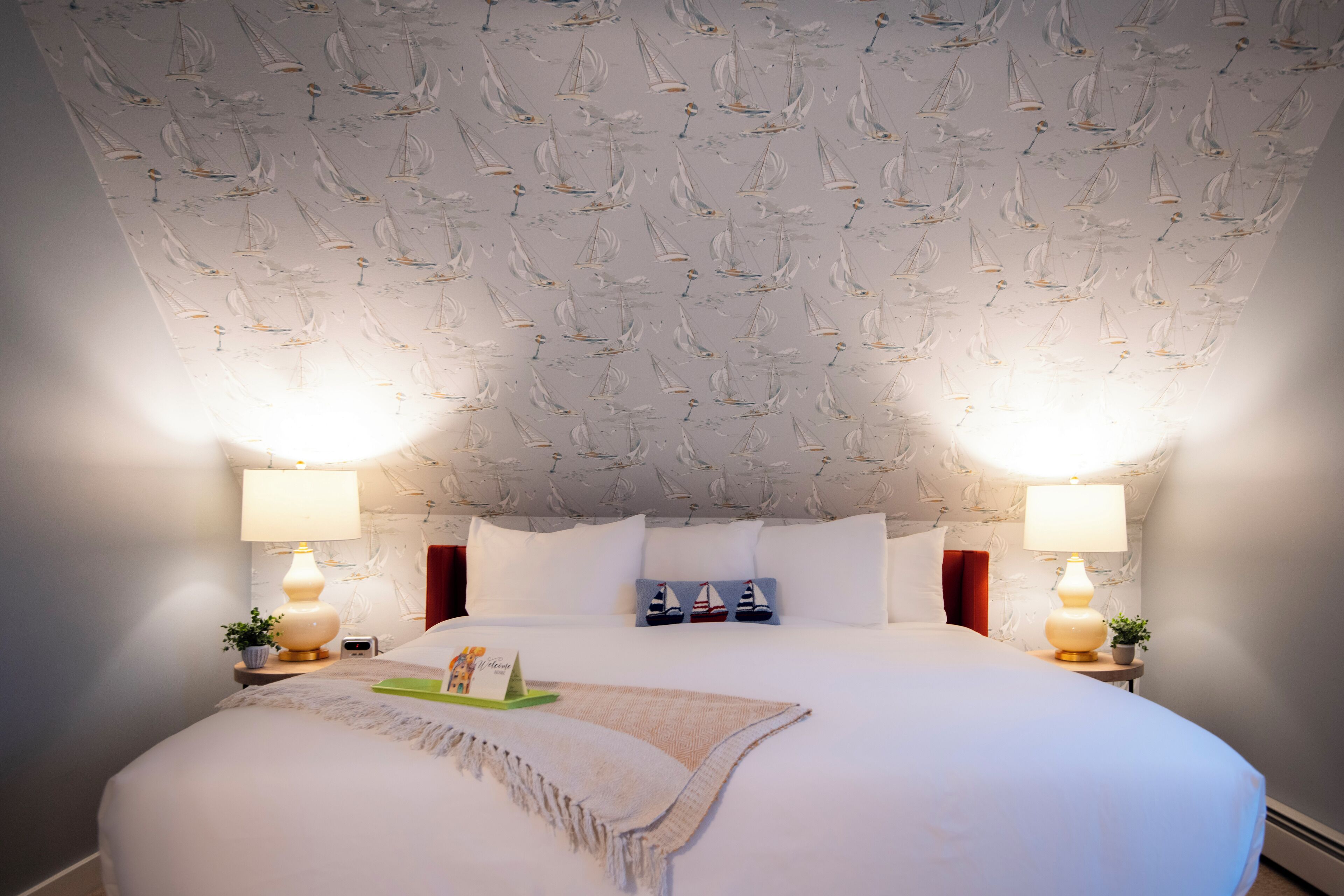 A neatly made bed with a white duvet, two bedside lamps, and a small plant on each side.