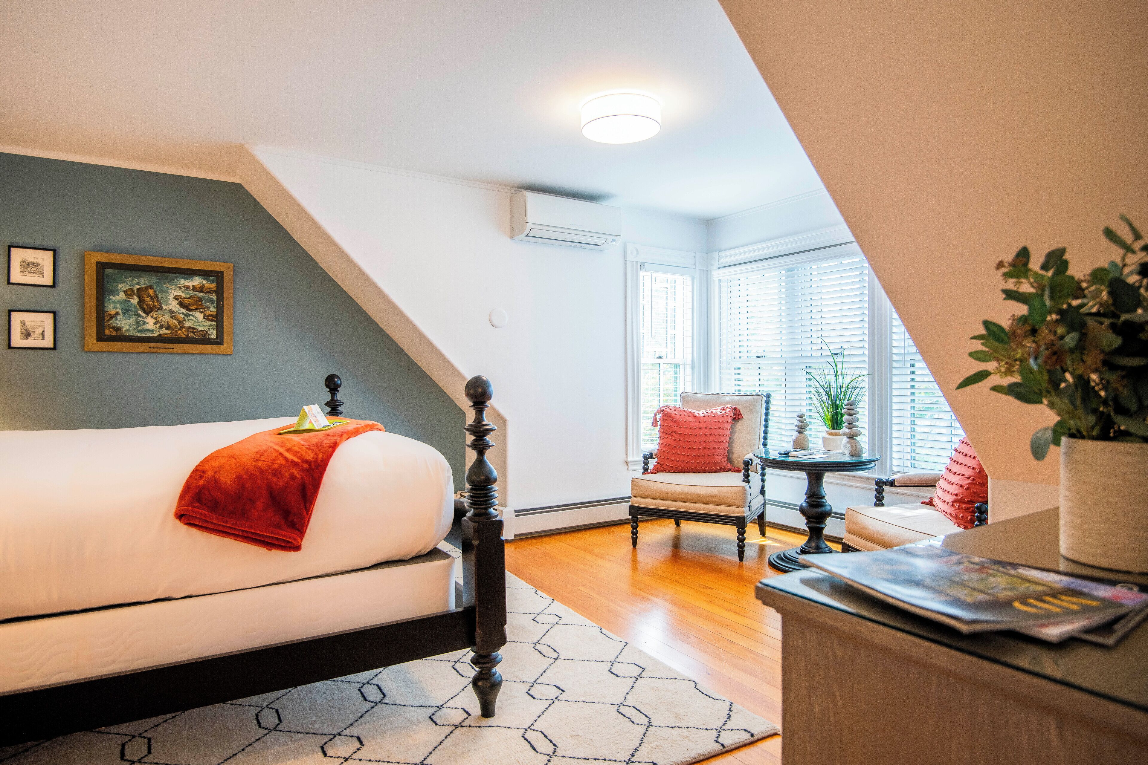 A bedroom with a bed, a chair, a small table, and a window with blinds.