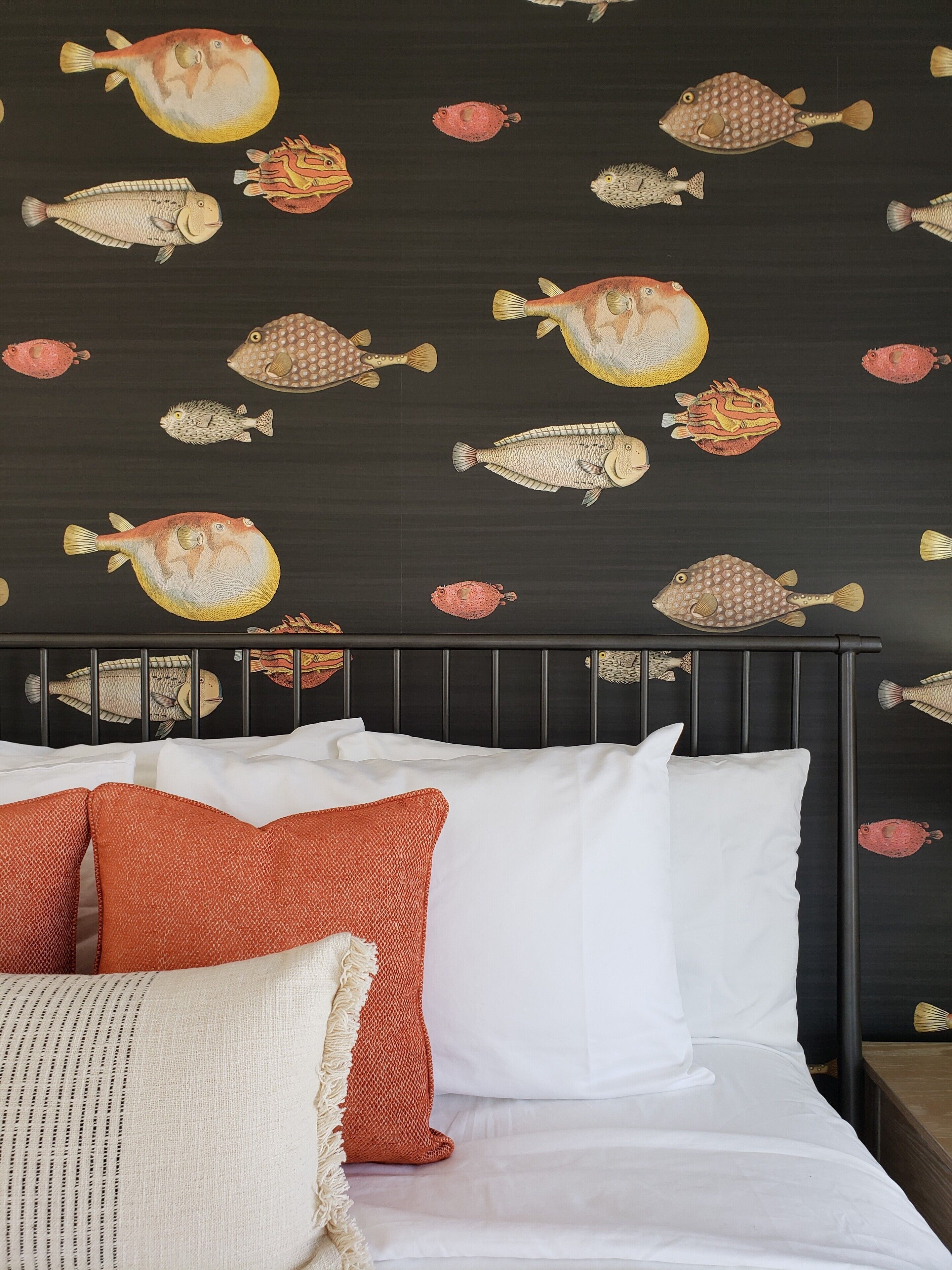 A bed with white and orange pillows, a dark headboard, and a wall with fish decals.