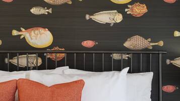 A bed with white and orange pillows, a dark headboard, and a wall with fish decals.