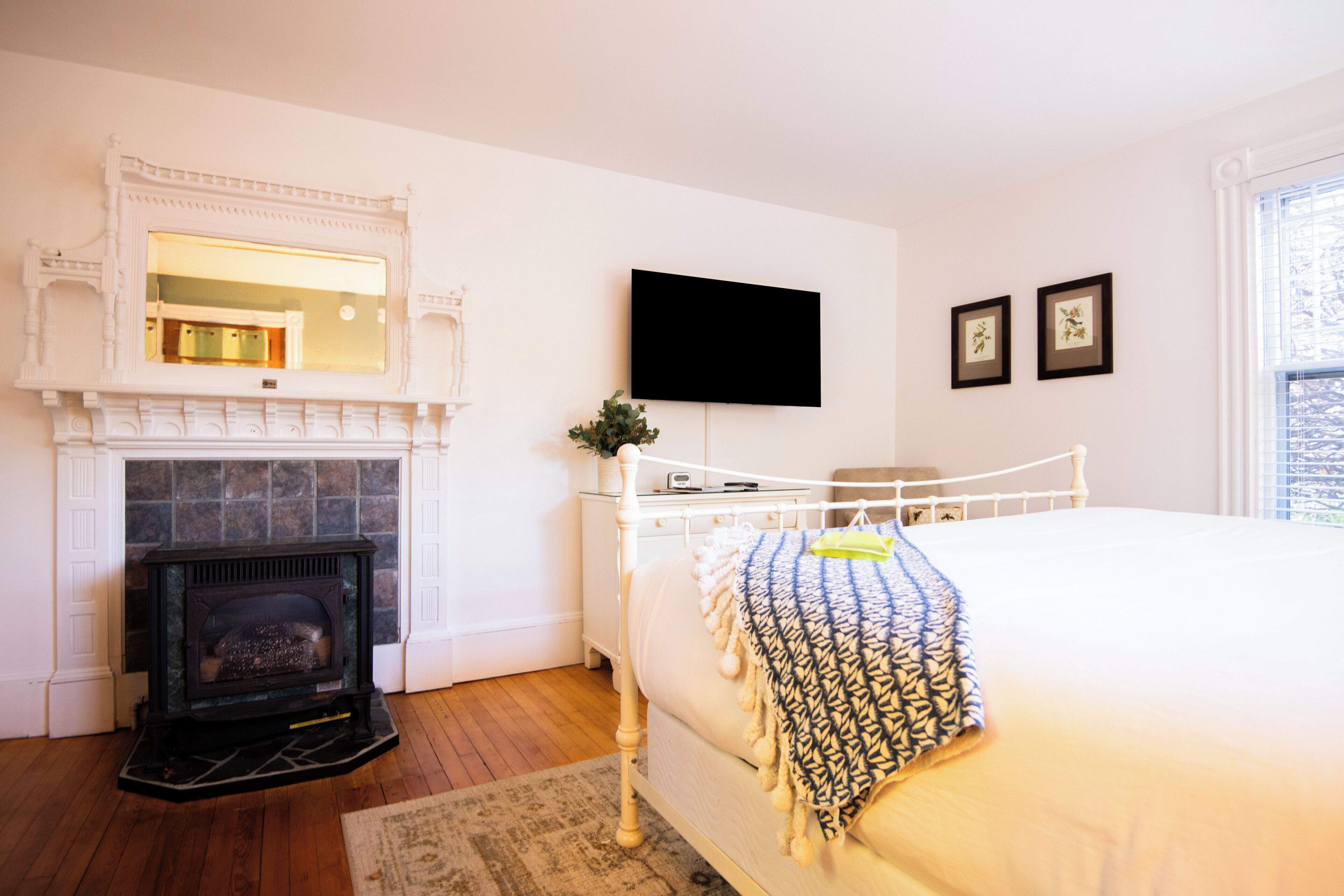 A bedroom with a fireplace, a bed, a TV mounted on the wall, and framed pictures.