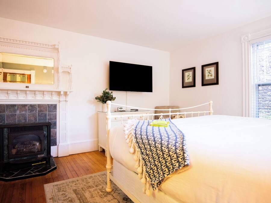 A bedroom with a fireplace, a bed, a TV mounted on the wall, and framed pictures.