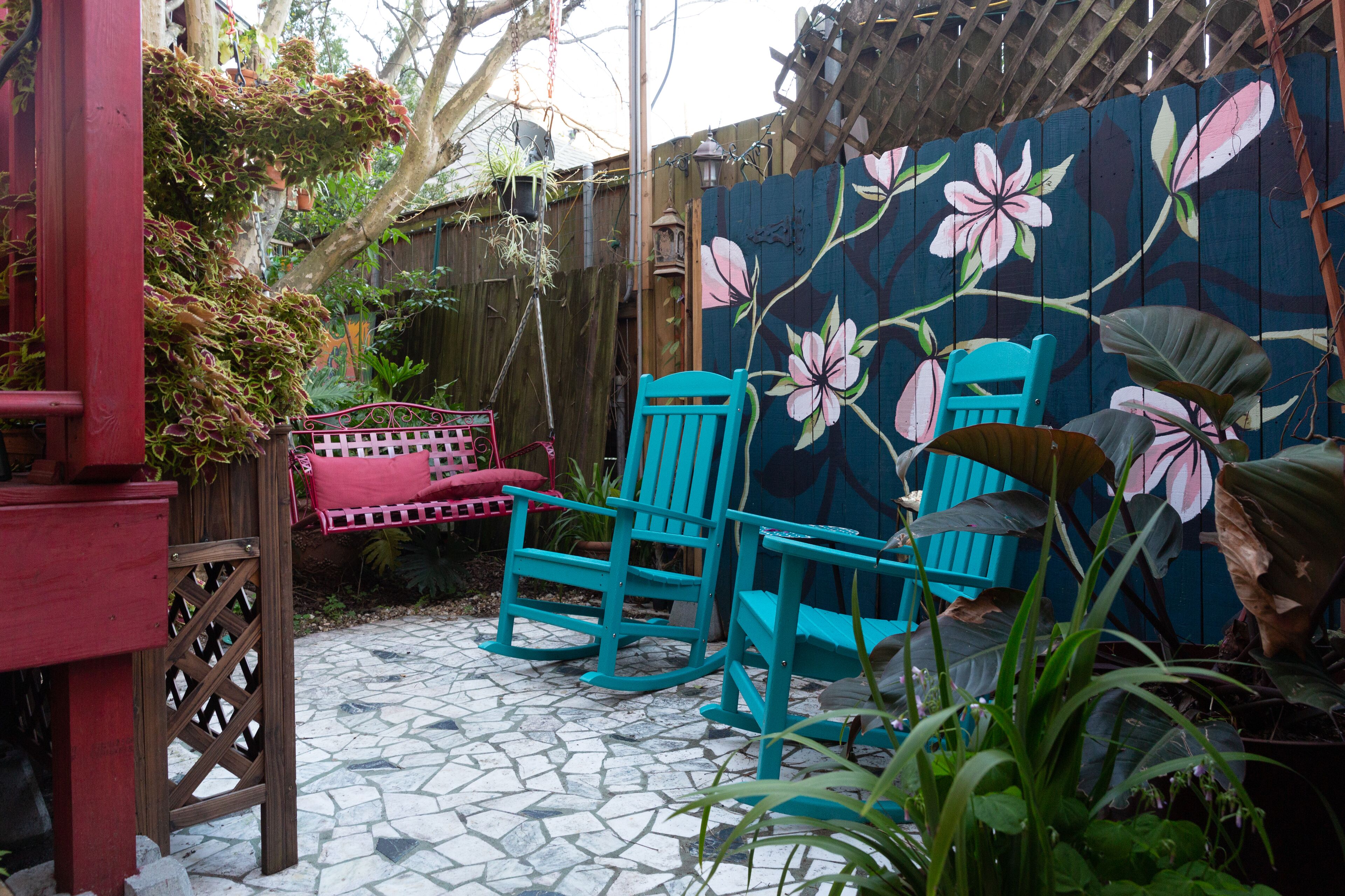 Een terras met twee turkoen zwenkstoelen, een rode bank en een houten omheining met een bloemenmuur.