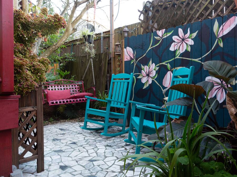 Een terras met twee turkoen zwenkstoelen, een rode bank en een houten omheining met een bloemenmuur.