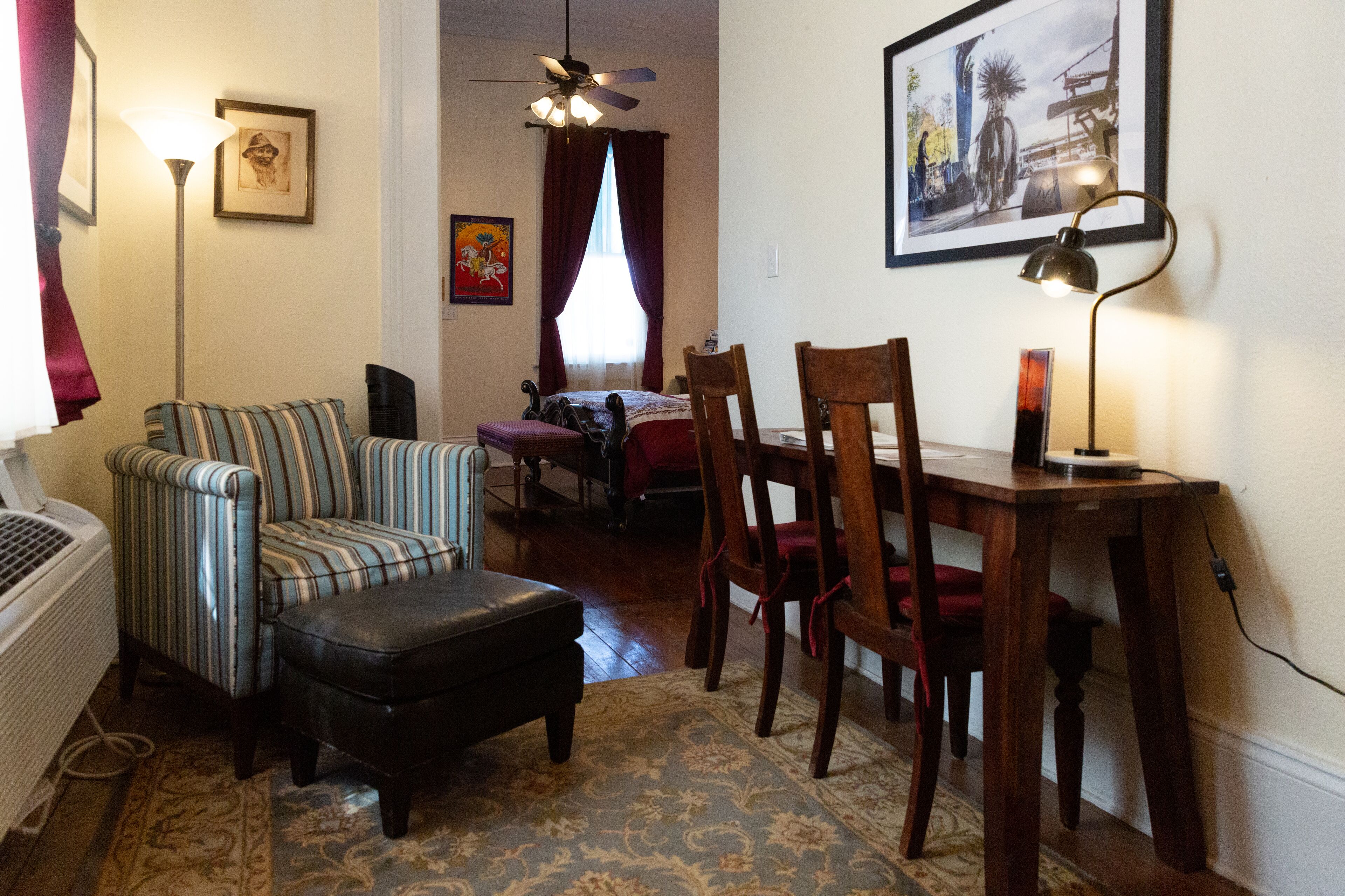A living room with a sofa, ottoman, and chairs, a dining table with chairs, a ceiling fan, and a framed picture on the wall.